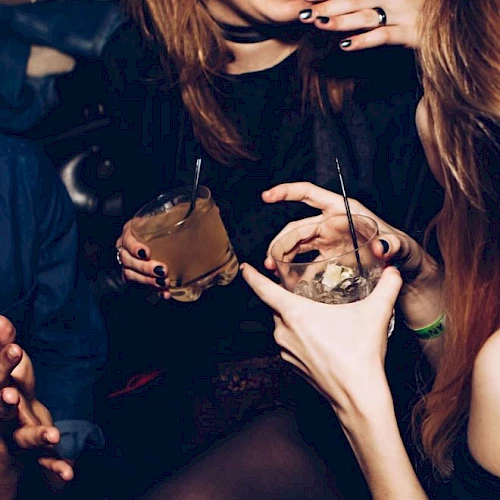 People are enjoying a night out, holding drinks and laughing, suggesting a lively social gathering.