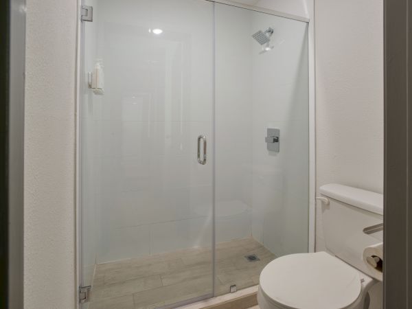 The image shows a bathroom with a glass-enclosed shower and a toilet next to it.